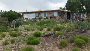 A stone house with a large patio area, surrounded by natural vegetation and trees. - Little Park Road Retreat - Hot Tub with a View (Grand Junction)