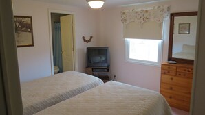 Une chambre avec deux lits, une commode, un téléviseur et une fenêtre ornée de rideaux à motifs floraux.