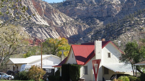 Une maison avec un toit rouge, un panneau indiquant « cédez le passage » et une montagne en arrière-plan.