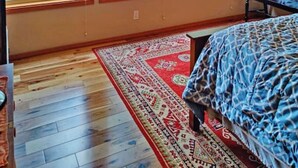 A bedroom with a large bed, a red chair, and a view of trees through three windows.