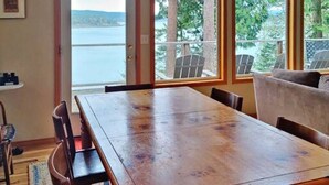 A dining area with a wooden table and chairs, large windows with a view of trees and a body of water.