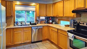 A kitchen with wooden cabinets, a stainless steel dishwasher, a black stove, and a window with blinds.