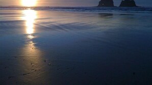 Una playa con atardecer, agua tranquila y dos formaciones rocosas.