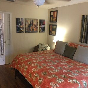 A bedroom with a floral-patterned bedspread, a cityscape painting, and a bamboo-themed painting on the wall.