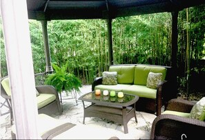 Un espace extérieur aménagé avec un canapé vert, des fauteuils en osier et une table basse avec un plateau en verre.