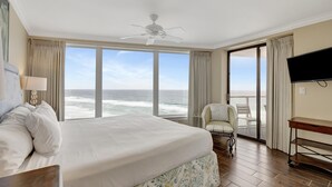 A hotel room with a large bed, a desk, a chair, a television, and a view of the ocean.