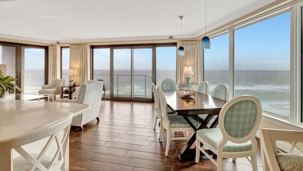 A spacious room with a large dining table, multiple chairs, and a view of the ocean through large windows.