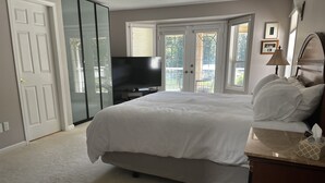 A bedroom with a large bed, a TV, a dresser, and a window with a view of the outdoors.
