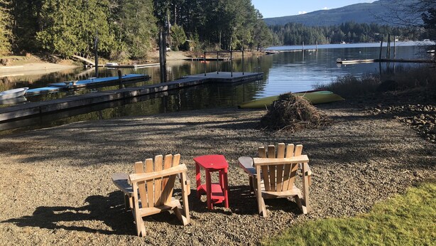 A lakeside setting with a dock, boats, and a picnic area with chairs and a table.