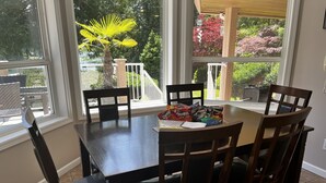 A dining area with a table and chairs, a window with a view of trees and a white railing.