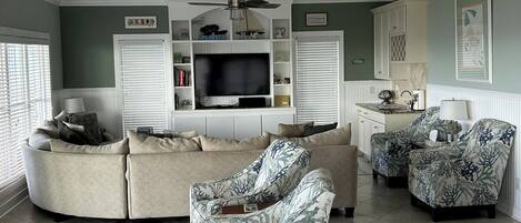 A living room with a sectional sofa, two patterned armchairs, a television, and a ceiling fan.