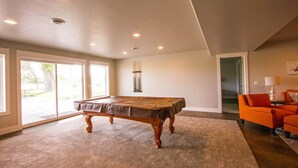 A spacious room with a pool table, large windows, and an orange armchair. - Huge Lakefront House - sleeps 22! Private Dock! Boating, Water Skiing, Rafting! (Heyburn)