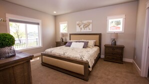 A bedroom with a large bed, two bedside tables, a window with a view, and a potted plant. - Huge Lakefront House - sleeps 22! Private Dock! Boating, Water Skiing, Rafting! (Heyburn)