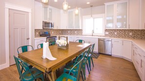 A modern kitchen with white cabinets, a wooden dining table, teal chairs, and pendant lighting. - Huge Lakefront House - sleeps 22! Private Dock! Boating, Water Skiing, Rafting! (Heyburn)