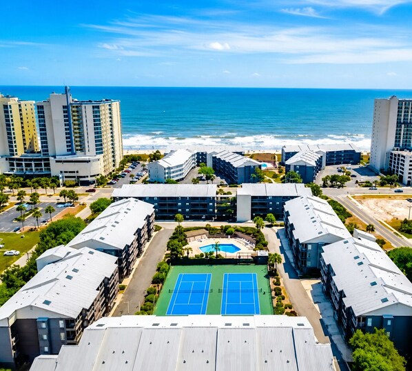 A high-rise hotel complex with multiple buildings, a tennis court, and a view of the ocean.