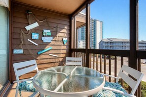 A balcony with a glass table and white chairs, a decorative wall with various signs, and a view of high-rise buildings.