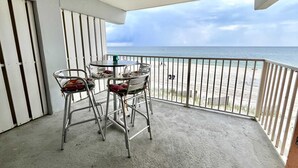 A balcony with metal chairs and a table, overlooking a beach with a railing.