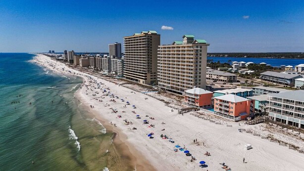 A coastal hotel with multiple floors, beachfront location, and a sandy beach with umbrellas.