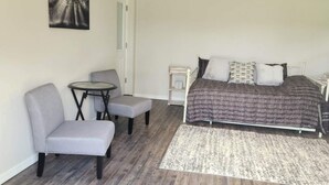 A bedroom with a bed, a ceiling fan, a small table with a chair, and a rug.