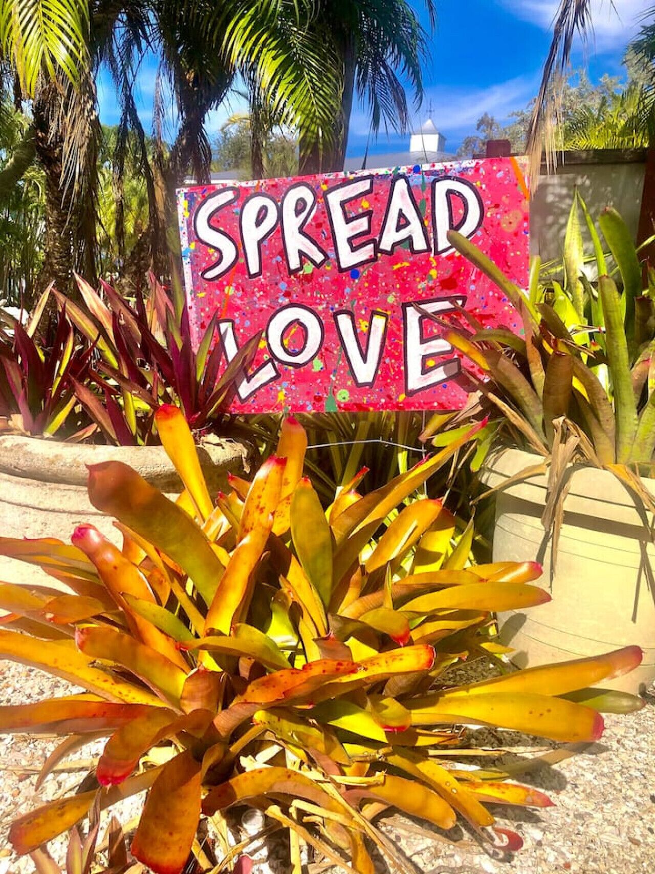 Un cartello con la scritta 'SPREAD LOVE' circondato da piante tropicali.