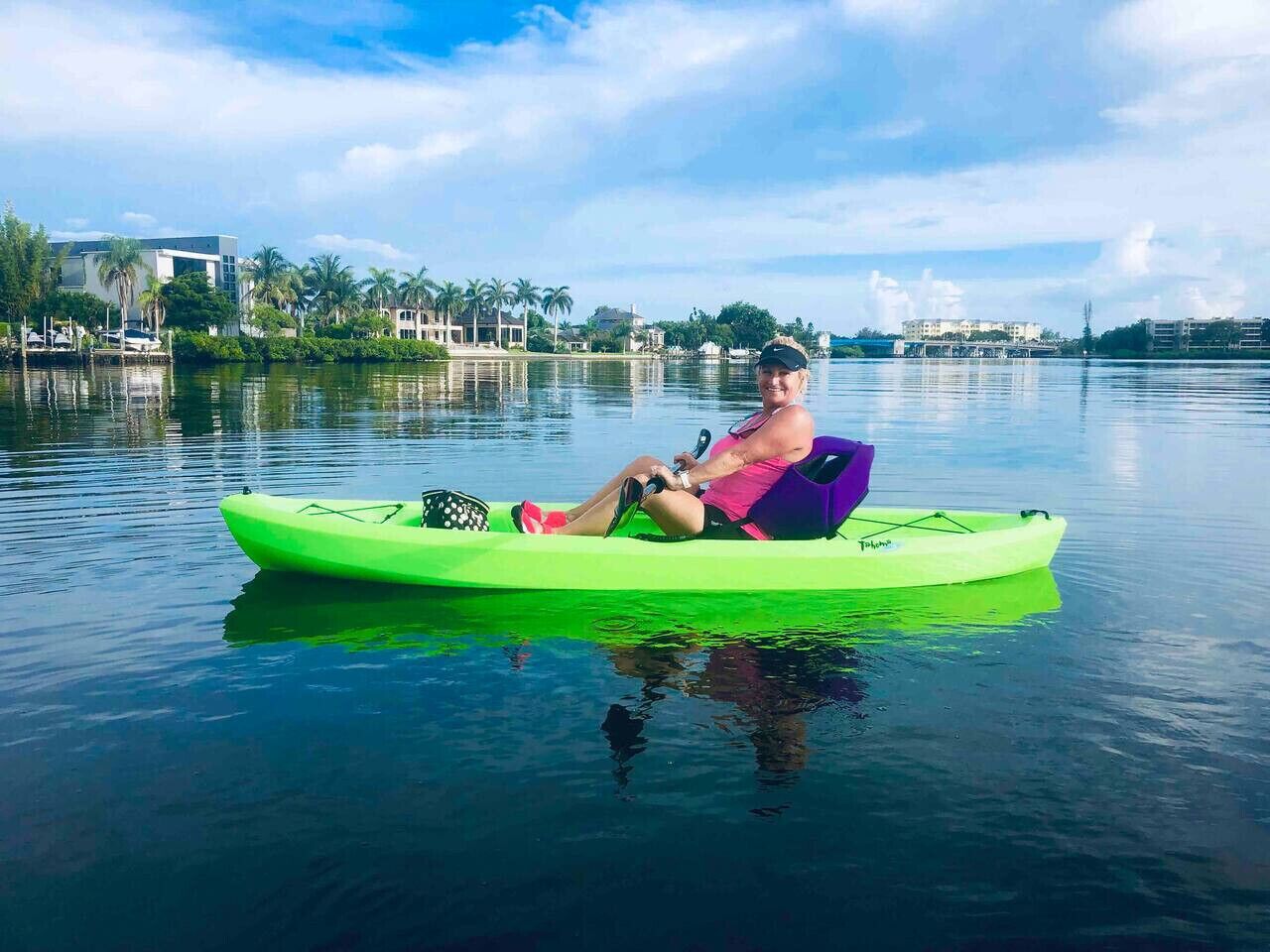 Una persona asseguda en una kayak verd brillant sobre aigua tranquil·la.