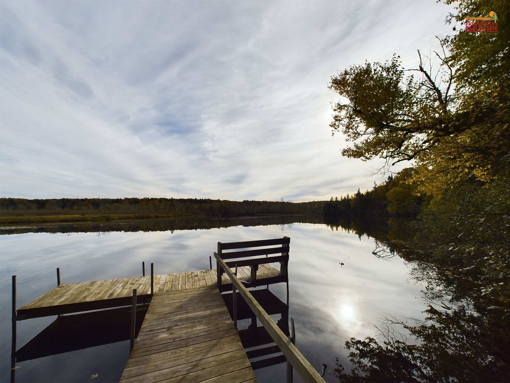 Une jetée en bois s’étendant sur un lac paisible, avec un banc à son extrémité.