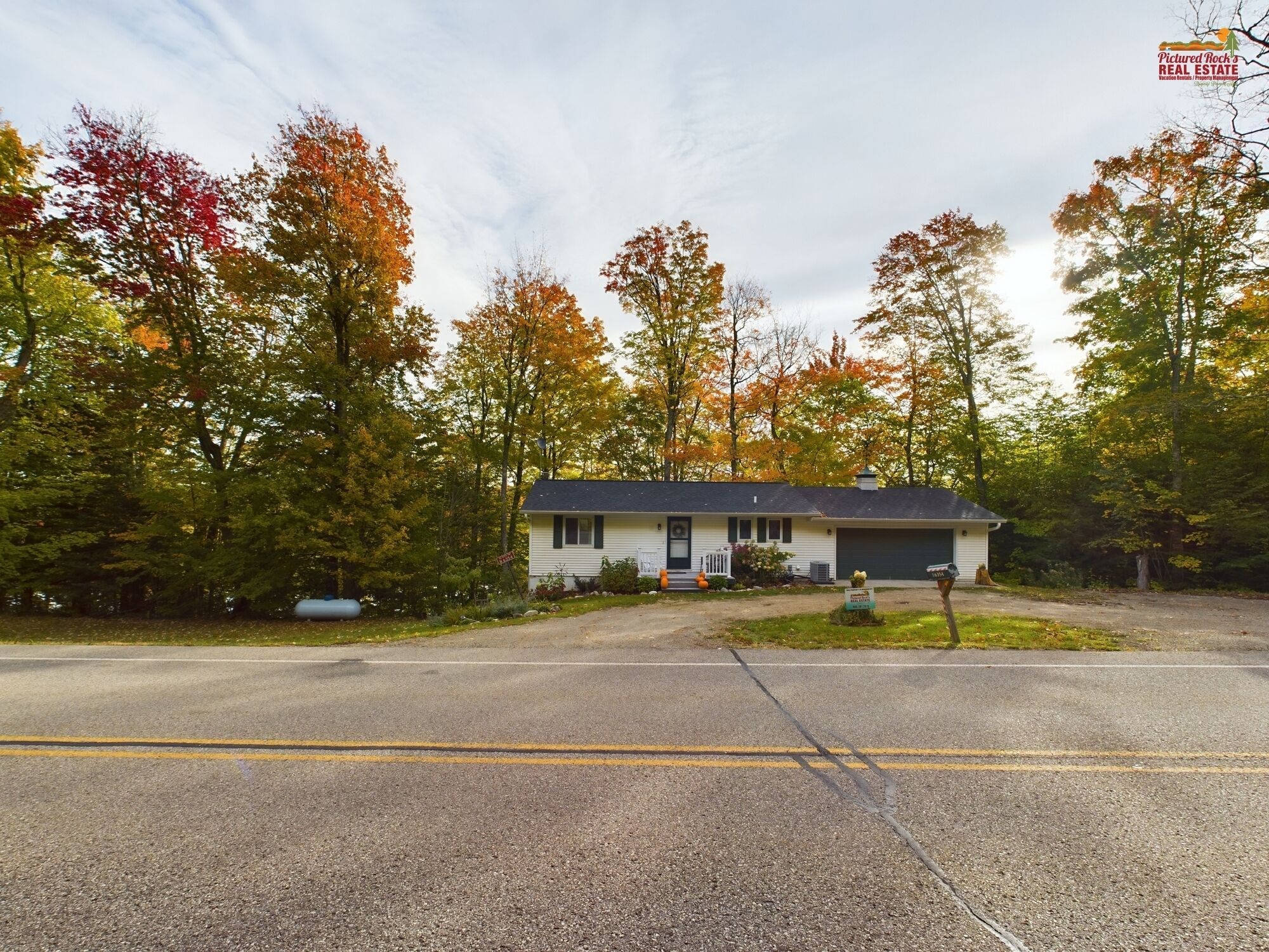 A single-story house with a garage, surrounded by trees with autumn foliage.