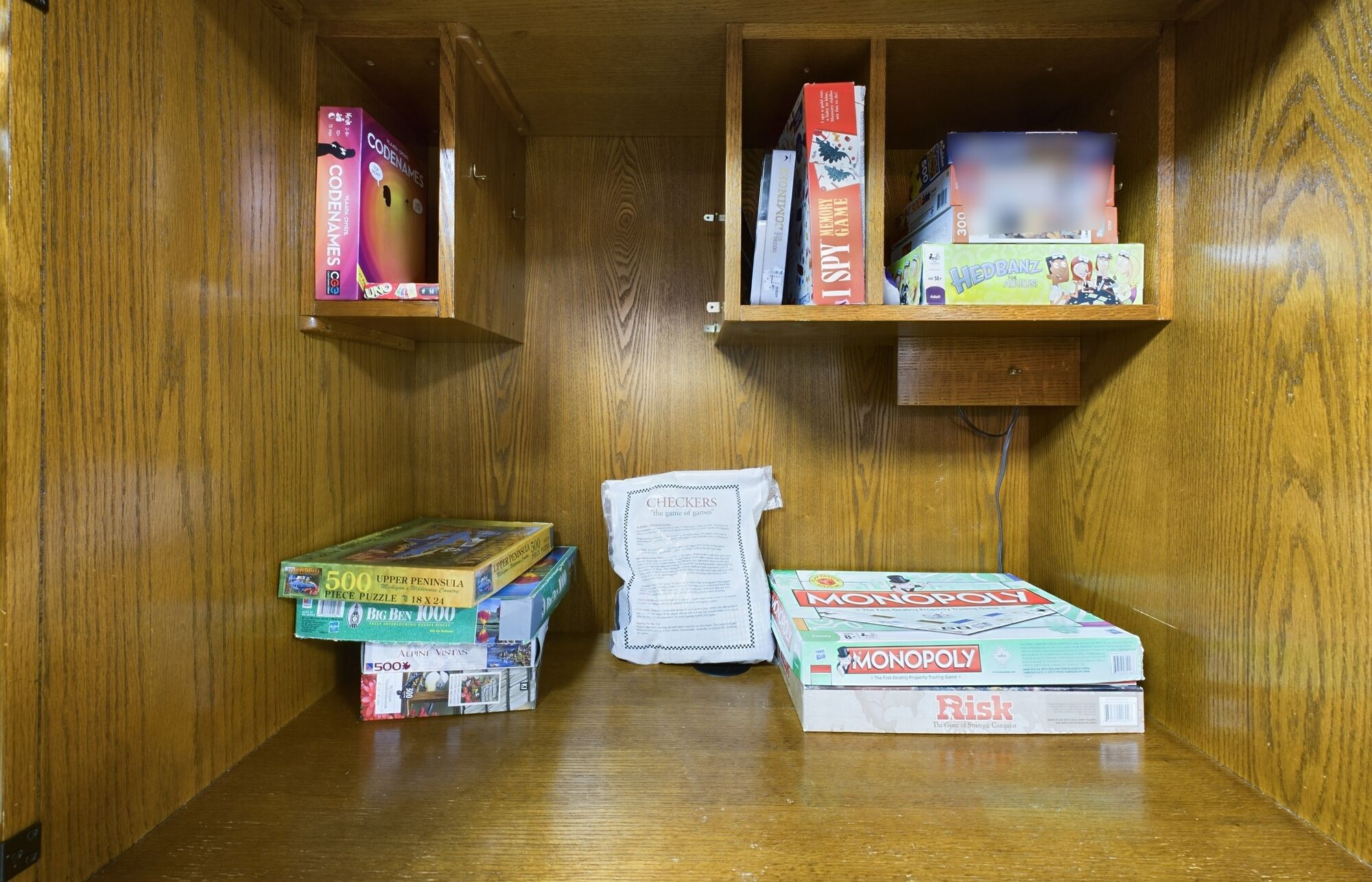 A wooden cabinet with shelves holding board games and puzzles.