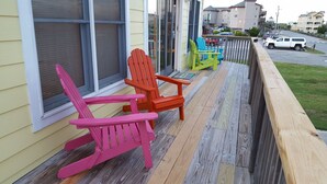 A porch with colorful Adirondack chairs and a wooden deck. - Barefootin' - steps from the beach, restaurants & shops. Very close to it all! (Kill Devil Hills)