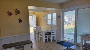 A dining area with a white table and chairs, a bench, and a colorful striped rug. - Barefootin' - steps from the beach, restaurants & shops. Very close to it all! (Kill Devil Hills)