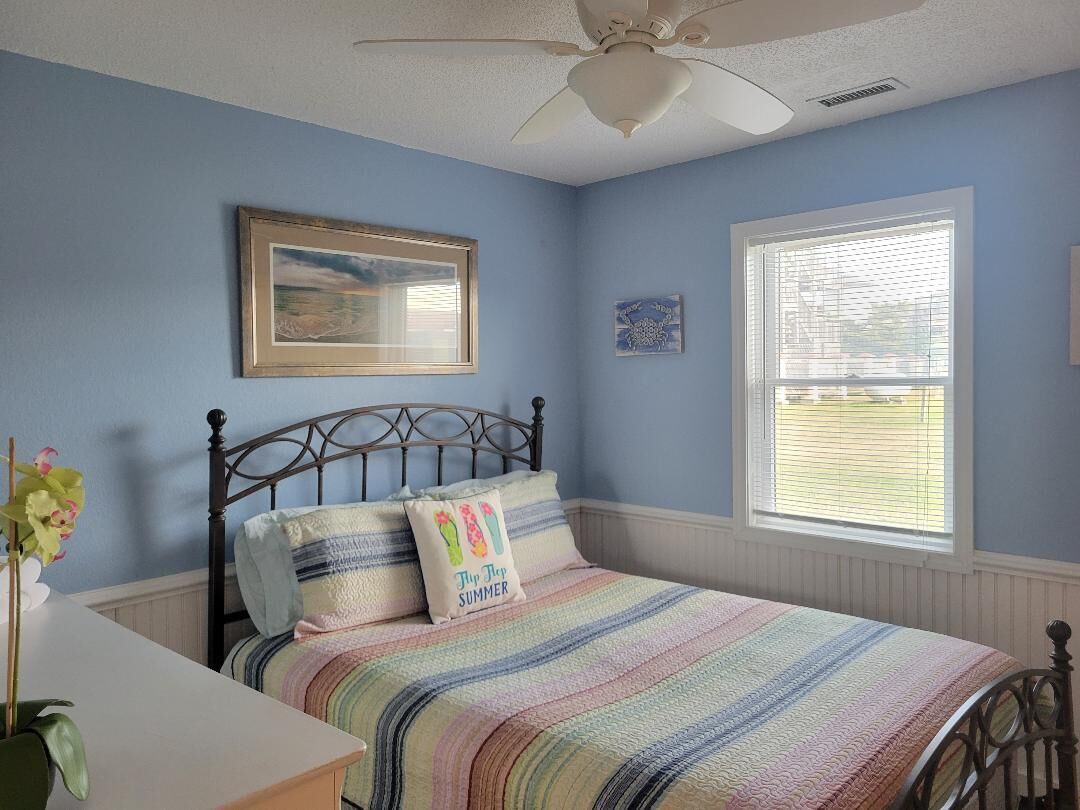 A bedroom with a bed, a ceiling fan, a window with blinds, and a framed picture on the wall.