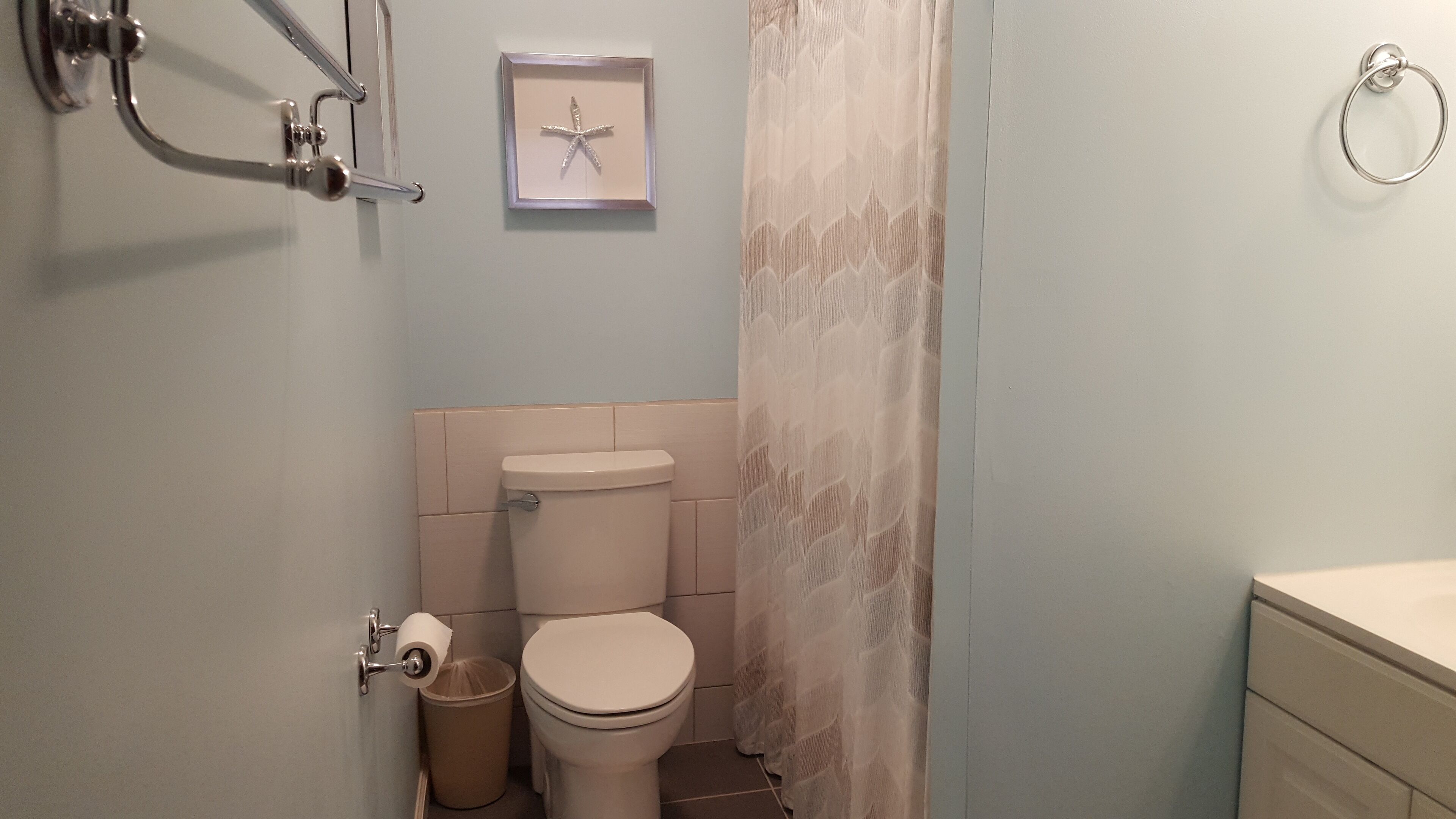 Ein Badezimmer mit Toilette, einem Mülleimer, einem Handtuchhalter und einem gerahmten Bild an der Wand.