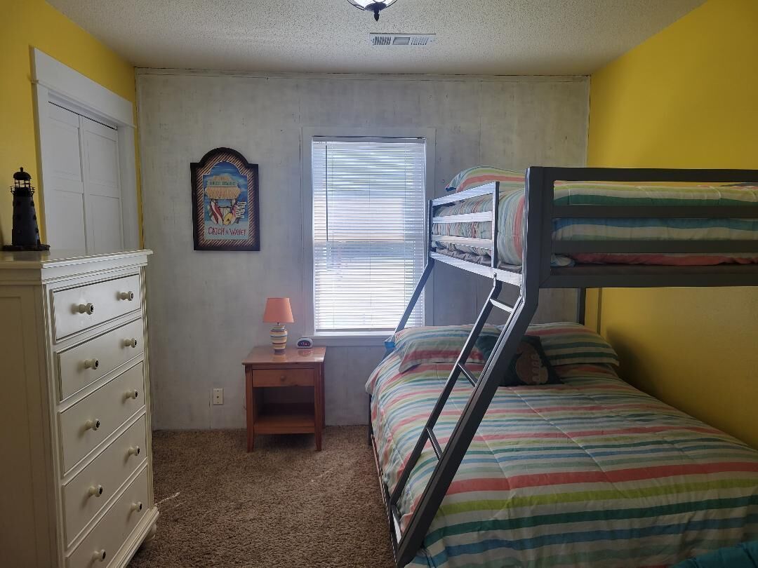 A bedroom with bunk beds, a dresser, a nightstand, a lamp, and a poster on the wall.