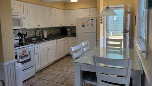 A kitchen with white cabinets, a microwave, a refrigerator, a glass dining table, and chairs. - Barefootin' - steps from the beach, restaurants & shops. Very close to it all! (Kill Devil Hills)