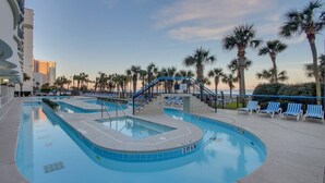 A pool area with multiple swimming pools, palm trees, and lounge chairs. - Meticulous Oceanfront 1Bedroom Suite/ Jetted tub! (Myrtle Beach)