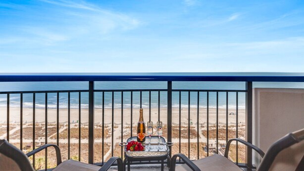 A balcony with a view of the beach, a table with a bottle and glasses, and a chair. - Meticulous Oceanfront 1Bedroom Suite/ Jetted tub! (Myrtle Beach)