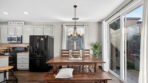 A modern kitchen with white cabinets, a black refrigerator, a wooden dining table, and a bench.
