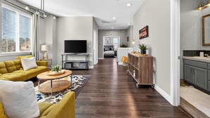 A modern living room with a sofa, coffee table, TV, and a kitchen area with cabinets and a countertop.