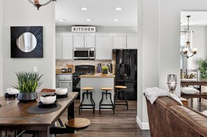 A modern kitchen with white cabinets, a central island with stools, a microwave, and a refrigerator.
