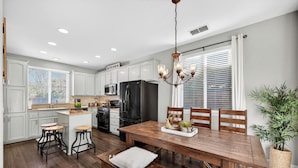 A modern kitchen with white cabinets, a black refrigerator, and a wooden dining table with chairs.