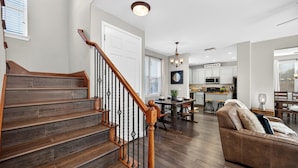 A spacious living area with a wooden staircase, a dining table, and a kitchen in the background.