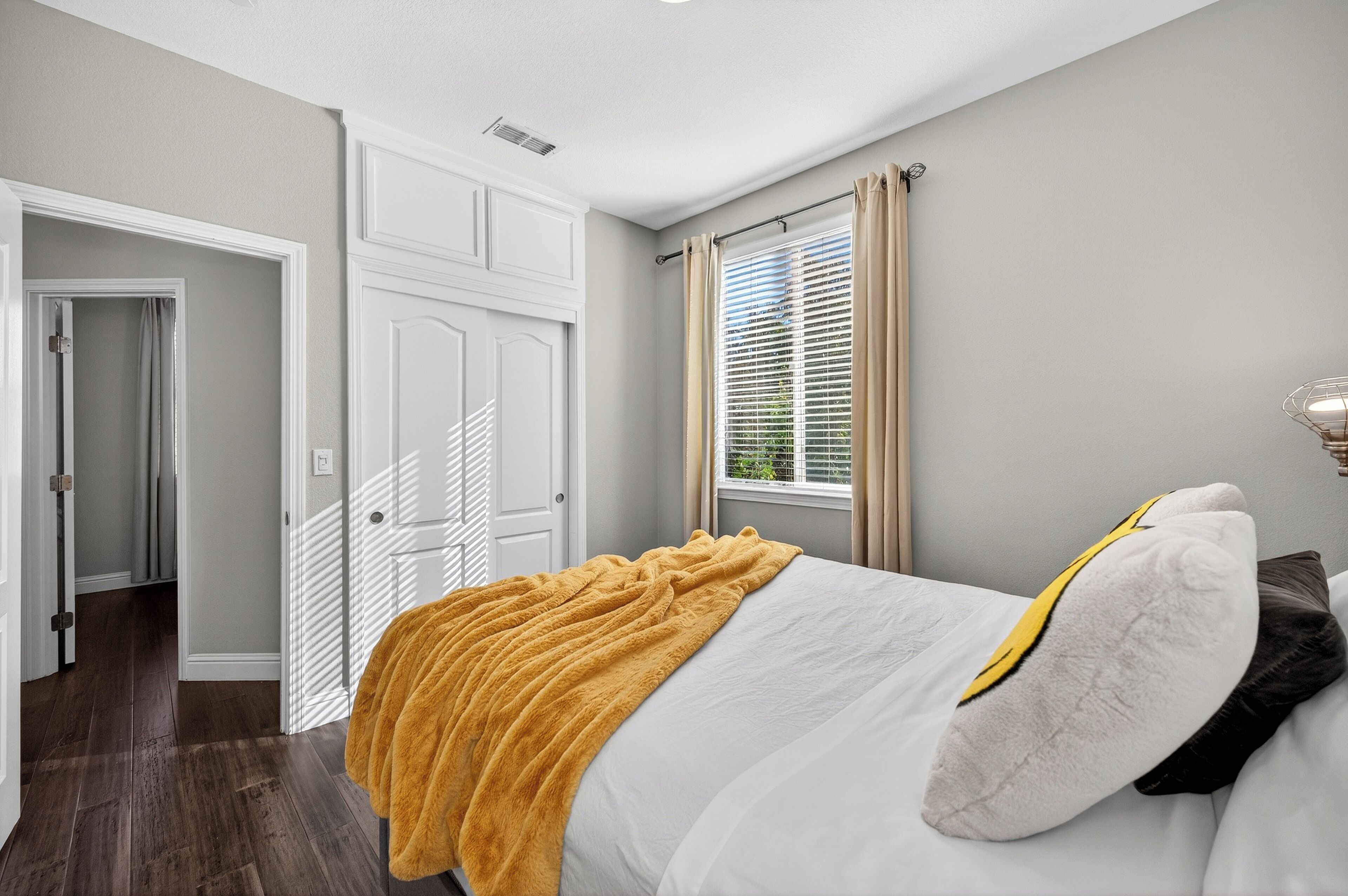 Un dormitorio con cama, ventana con cortinas, una puerta y un pasillo.