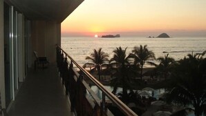 Ein Balkon mit Blick auf den Sonnenuntergang über dem Meer, Palmen und einen Poolbereich.