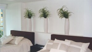 Ein Hotelzimmer mit zwei Betten, einem Nachttisch und drei Kübelpflanzen an der Wand.