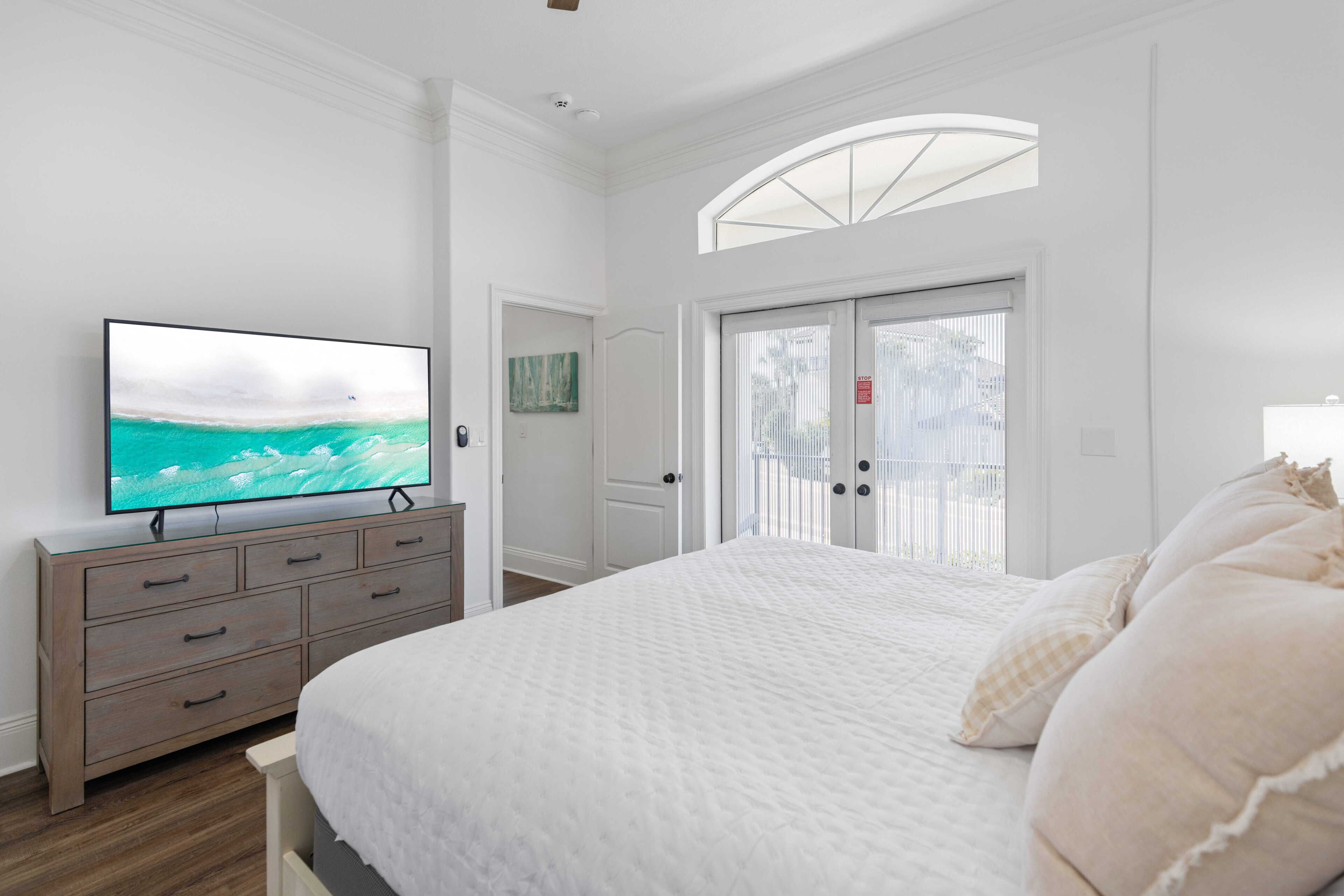 A bedroom with a bed, a TV on a dresser, a door with a view, and a window.