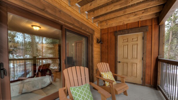 A wooden porch with two Adirondack chairs, one with a green pillow and the other with a yellow pillow. - In Town Vacation Rental within Walking Distance to Slopes, Bike Trails & Main St (Breckenridge)