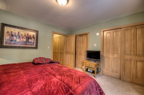 A bedroom with a red bedspread, a television on a wooden stand, and wooden wardrobes. - Vacation Rental within Walking Distance to Slopes, Main St. #0433770002 (Breckenridge)