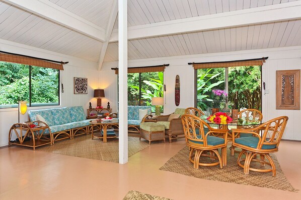 A spacious room with a large window, a sofa, a dining table with chairs, and a decorative wall piece.