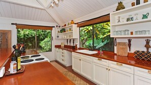 Una cocina con armarios blancos, encimera de madera y ventana con vistas a la vegetación.