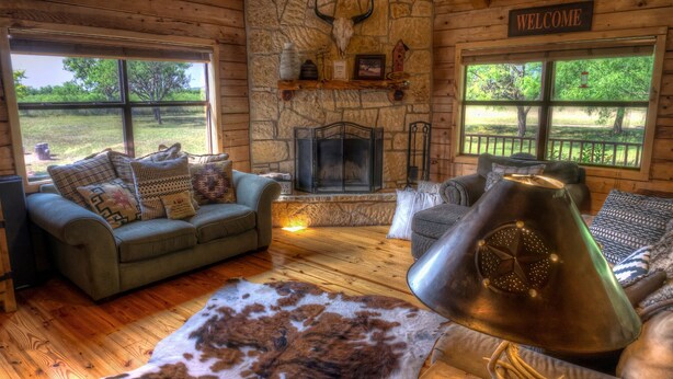 Interior acogedor de una cabaña con chimenea, paredes de madera y un cartel que dice 'WELCOME'.